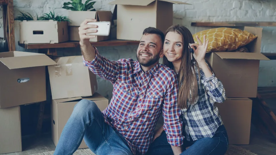 A couple taking a selfie with their new house keys among moving boxes